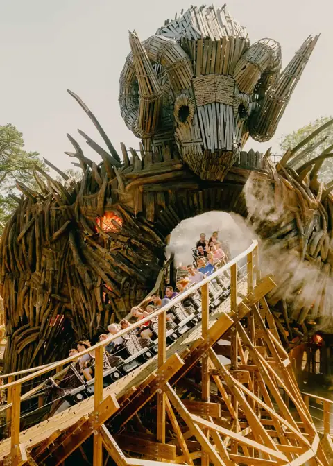 Guests riding a wooden coaster through a large dragon-themed structure.
